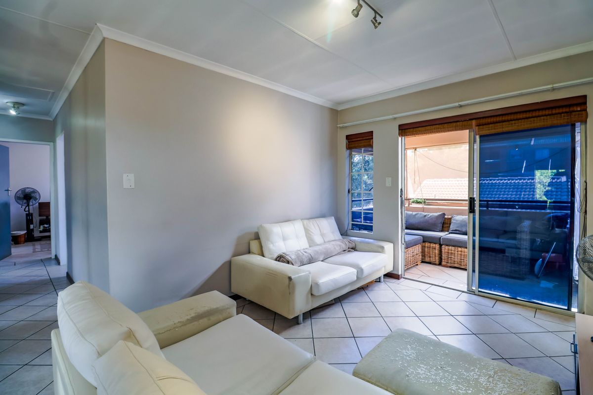 A living room featuring ceramic floor tiles, track lighting, and a sliding glass door providing access to an outdoor balcony area.