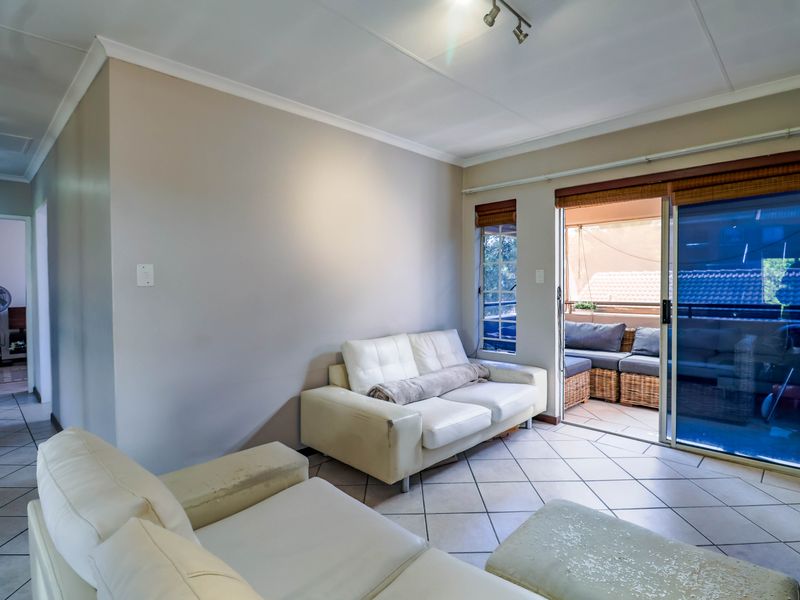 A living room featuring ceramic floor tiles, track lighting, and a sliding glass door providing access to an outdoor balcony area.