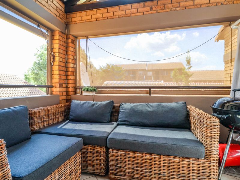 A covered balcony featuring exposed brick walls, a metal balustrade, and retractable sun blinds, offering a functional outdoor living space.