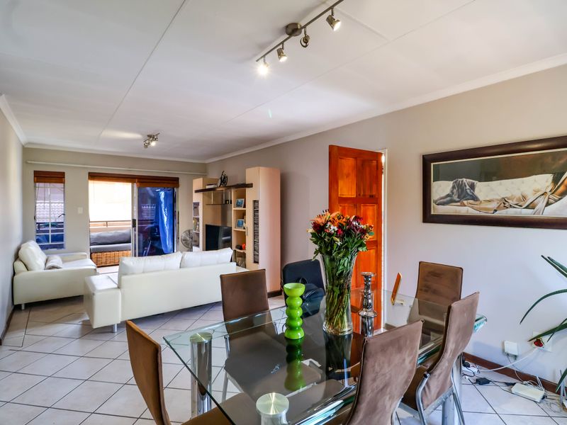 Spacious open-plan living and dining area featuring tiled flooring, track lighting, and direct access to an outdoor balcony through sliding glass doors.