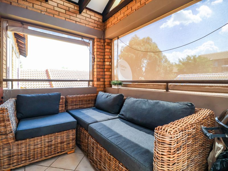 A covered balcony featuring exposed brick walls, tiled flooring, and retractable sun blinds, providing a comfortable outdoor living space.