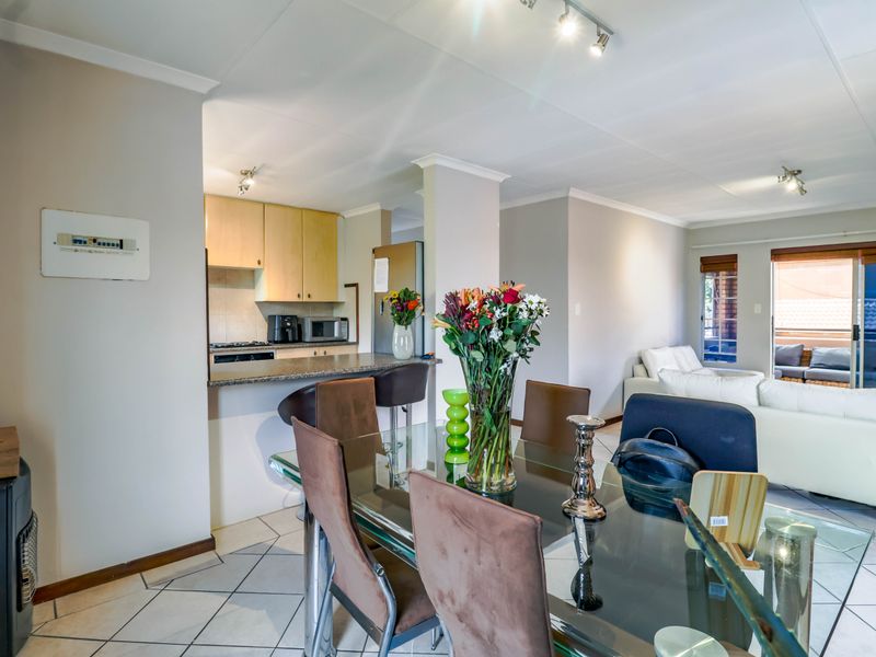 Open-plan living and dining area featuring a functional kitchen with granite countertops, tiled flooring, and direct access to a balcony through sliding glass doors.