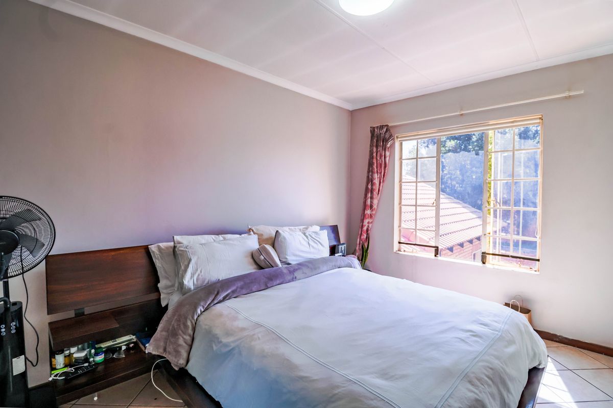 A bedroom featuring tiled flooring and a window with security bars, providing natural light and a view of the surrounding area.