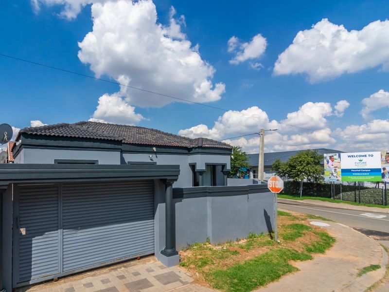 Front exterior view of a modern house featuring a grey perimeter wall, tiled roof, and a secure roller garage door.
