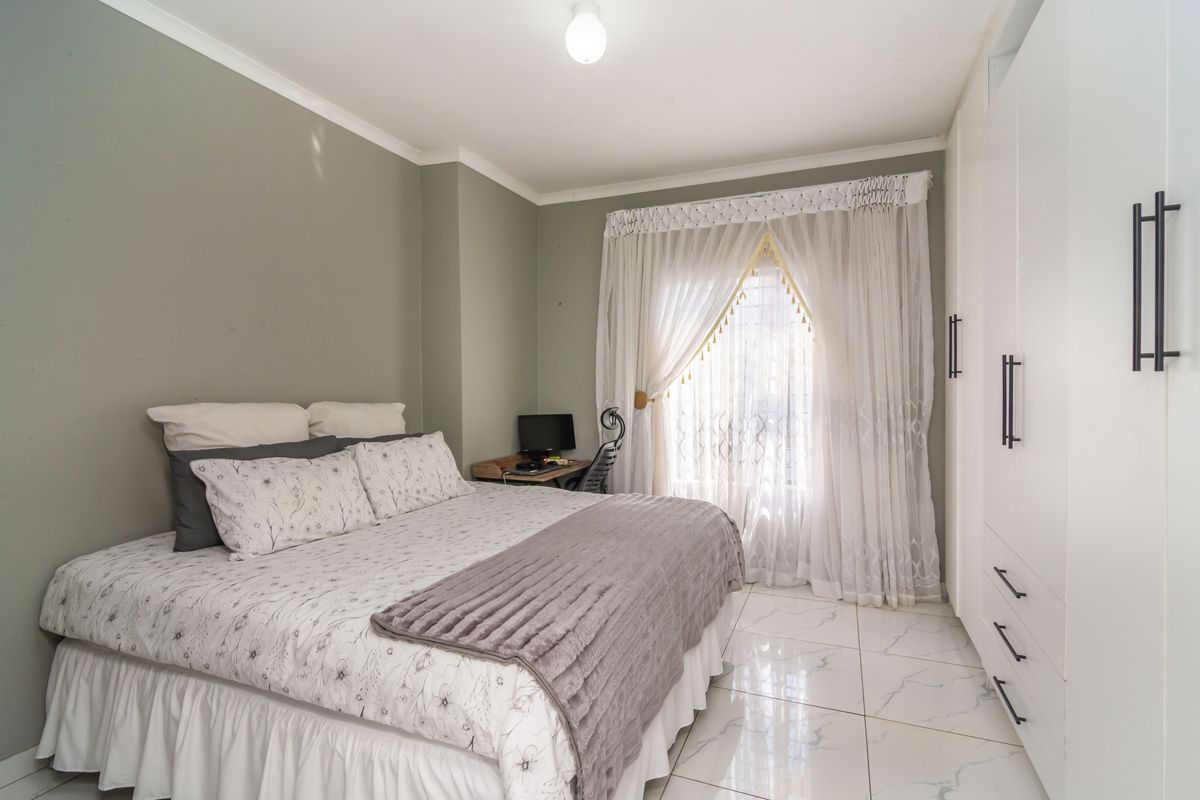 A well-maintained bedroom featuring modern white built-in cupboards, polished marble-look floor tiles, and neutral wall tones.