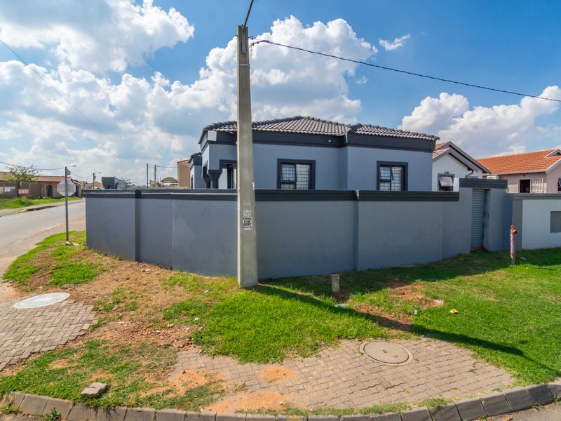 Street view of a residential property featuring a grey perimeter wall, tiled roof, and security bars on the windows.