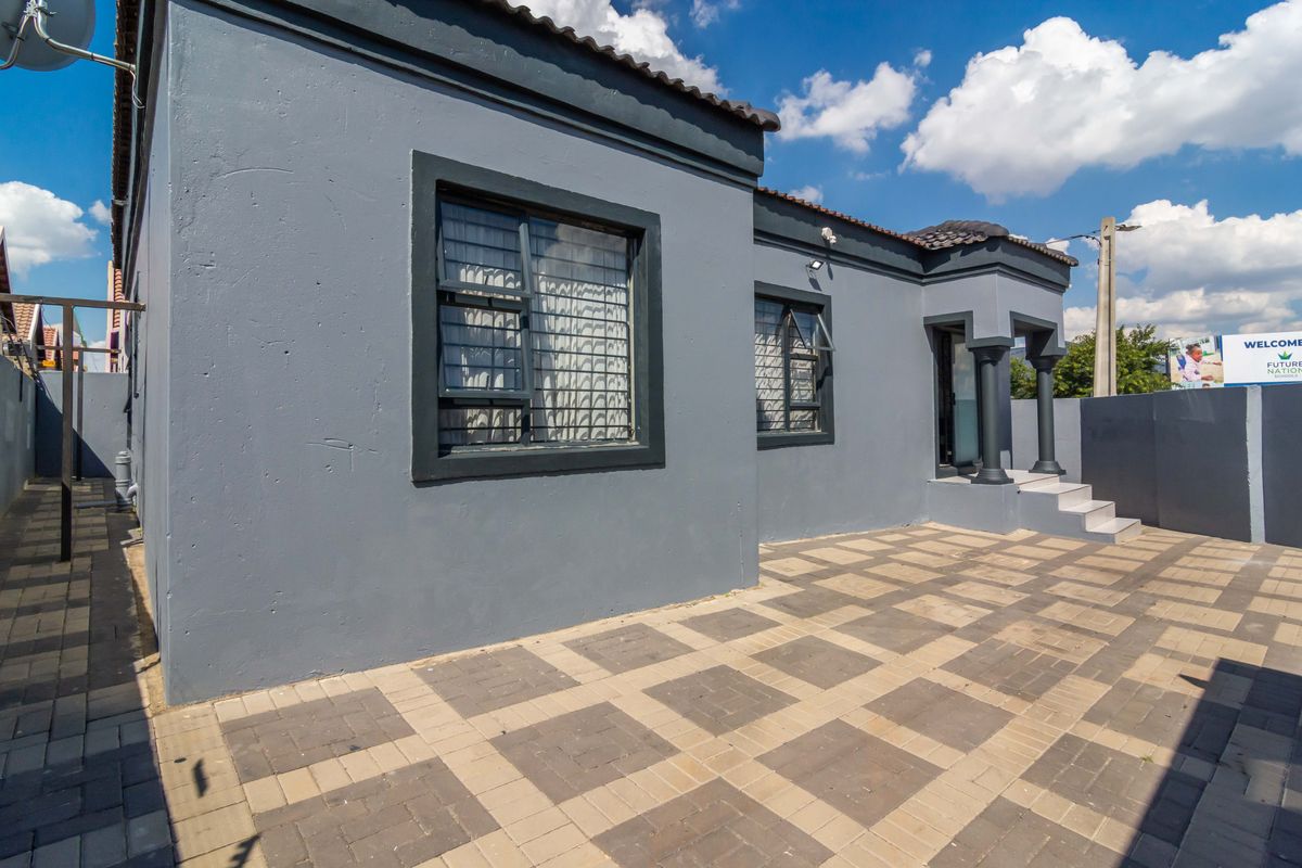 A well-maintained rear exterior view featuring a paved patio area, dark grey rendered walls, and secure window fittings.