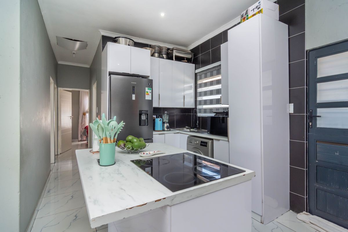 Modern kitchen featuring white cabinetry, a marble-look island with an integrated induction hob, and black tiled splashbacks.