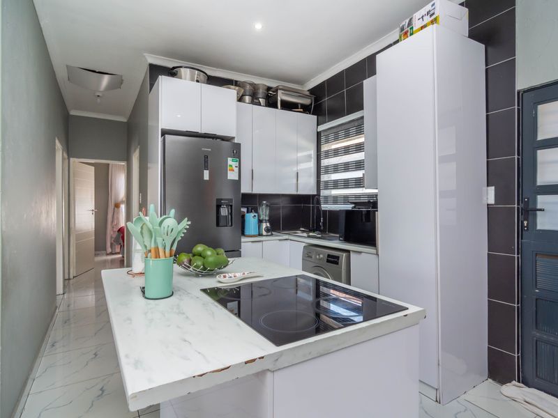 Modern kitchen featuring white cabinetry, a marble-look island with an integrated induction hob, and black tiled splashbacks.