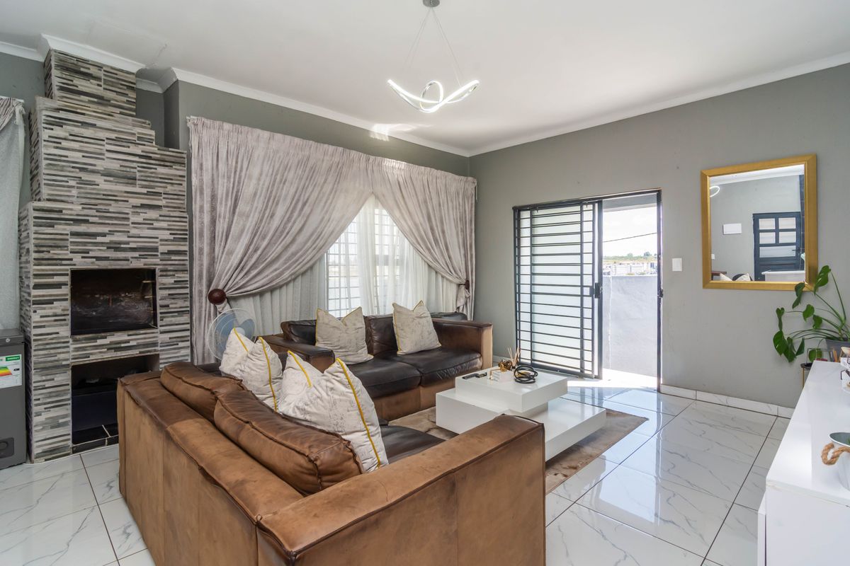 A well-maintained living room featuring polished marble-look floor tiles, a striking stone-clad built-in fireplace, and direct access to an outdoor area via a sliding door.