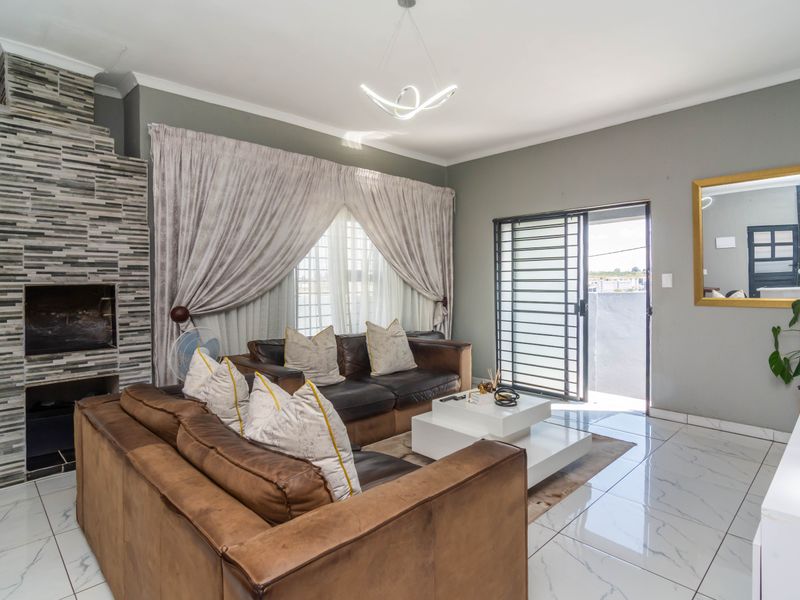 A well-maintained living room featuring polished marble-look floor tiles, a striking stone-clad built-in fireplace, and direct access to an outdoor area via a sliding door.