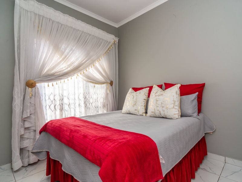 A well-maintained bedroom featuring neutral grey walls, tiled flooring, and decorative window treatments.