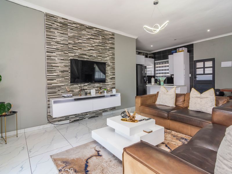 Open-plan living area featuring a modern tiled floor, a decorative stone-look feature wall with a floating console, and an integrated kitchen space.