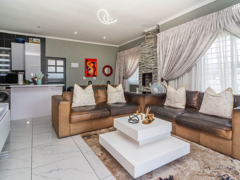Open-plan living area featuring marble-look floor tiles, a stone-clad fireplace, and an integrated kitchen space with modern cabinetry.