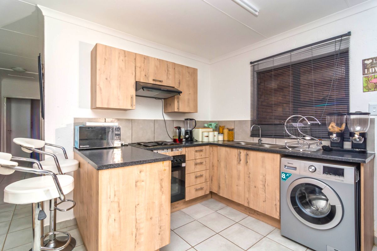 Compact kitchen featuring light wood-look cabinetry, dark countertops, tiled backsplash, and integrated space for a washing machine.