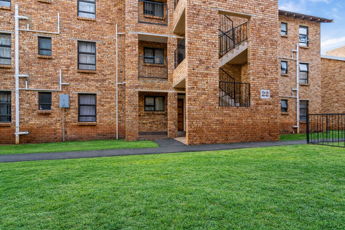 Exterior view of a multi-story brick apartment building featuring external staircases, metal railings, and a shared lawn area.