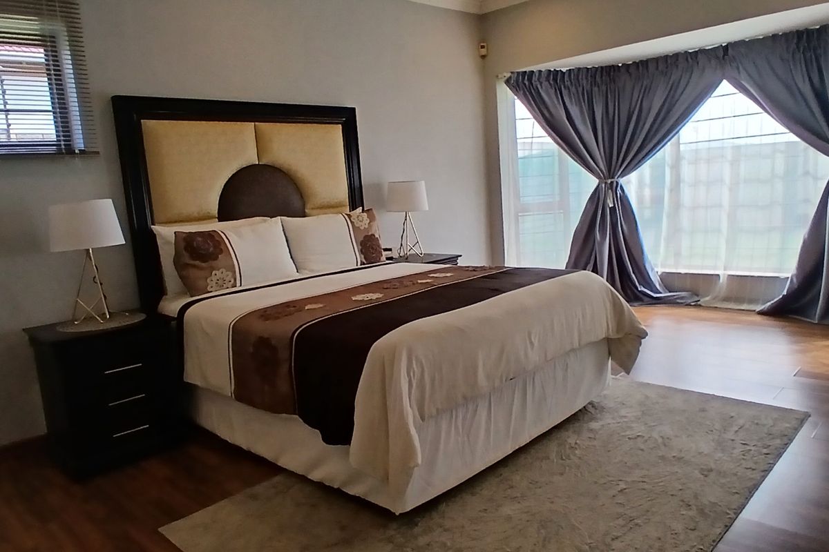 Spacious bedroom featuring wood-look flooring, large windows with curtains, and a neutral color palette, providing a comfortable and well-lit living space.