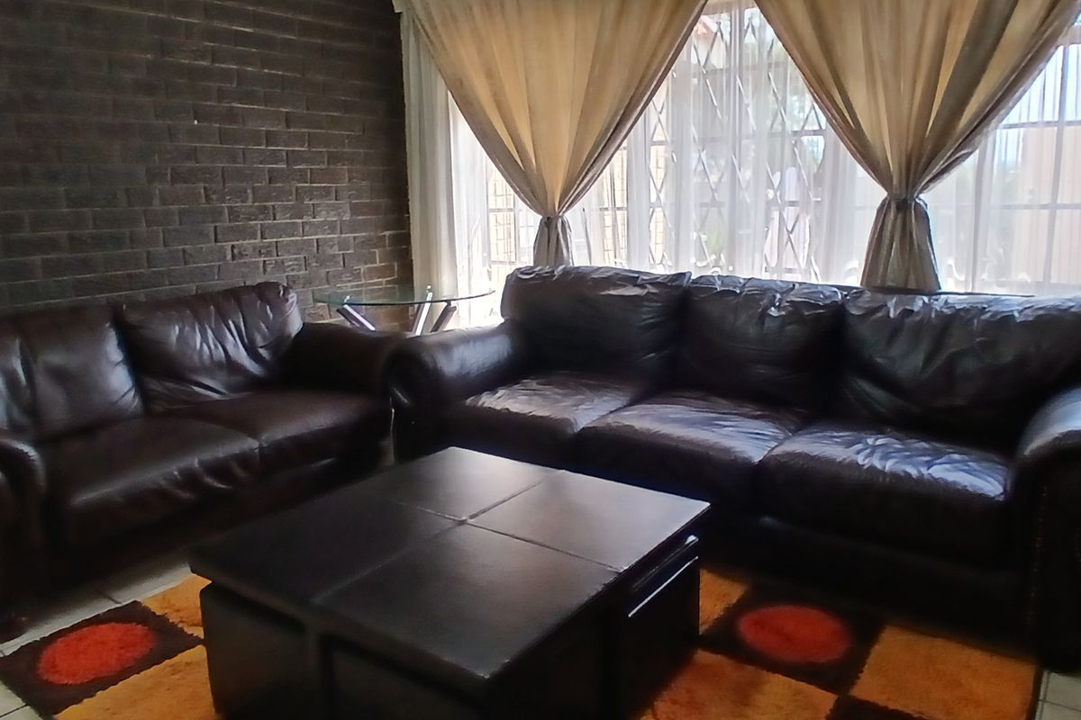 A living room featuring a dark brick accent wall, tiled flooring, and large windows with security bars.