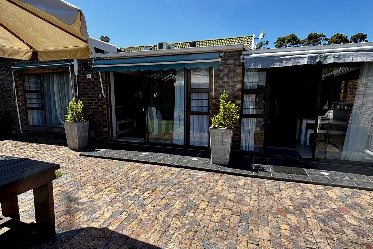 A paved rear courtyard featuring brickwork, retractable awnings, and large sliding glass doors providing seamless access to the interior living spaces.