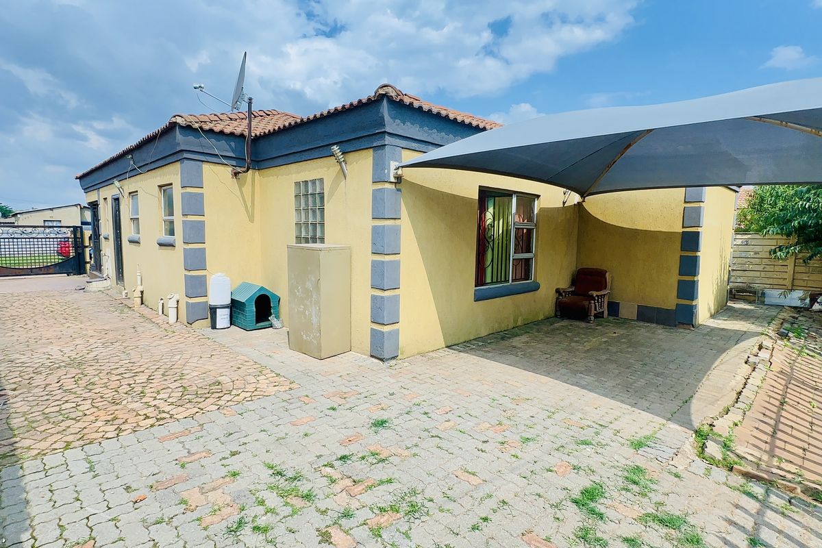 Rear exterior view of the house featuring a paved driveway, a shade sail structure, and a secure gated entrance.