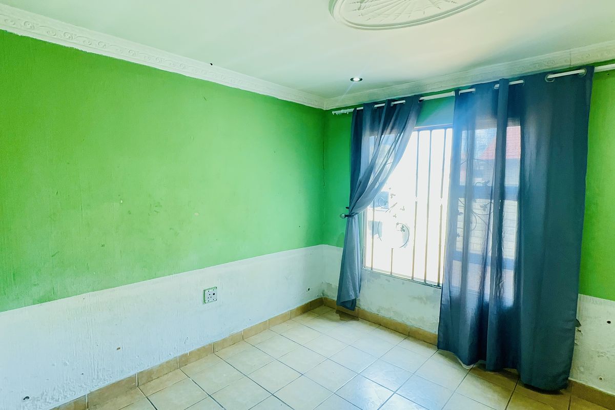 An empty bedroom featuring tiled flooring, security bars on the window, and decorative ceiling coving, requiring cosmetic updates to the wall finishes.