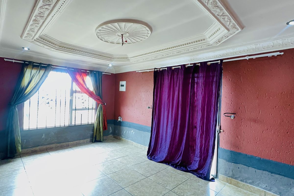 An empty living room featuring decorative ceiling molding, ceramic floor tiles, and security bars on the windows, requiring cosmetic updates to the wall finishes.
