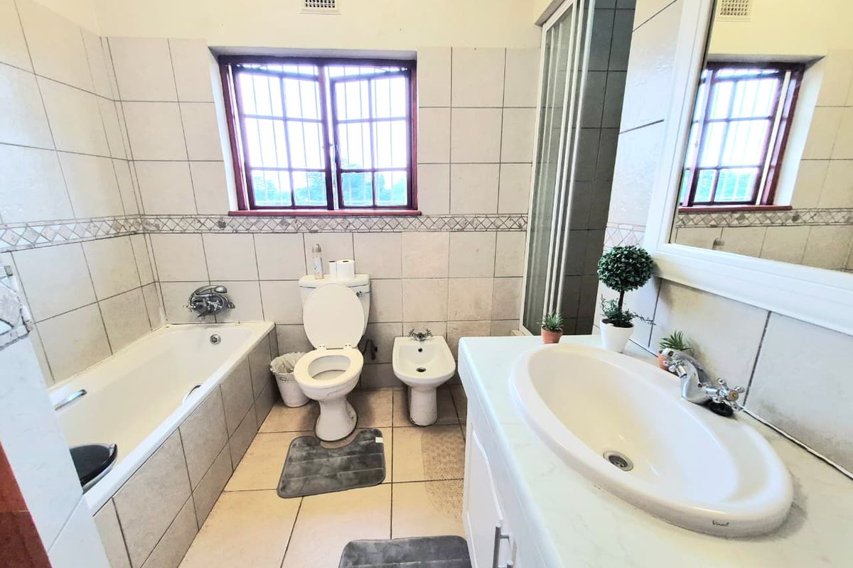 A functional bathroom featuring a bathtub, separate shower, toilet, bidet, and a vanity basin with neutral wall and floor tiling.