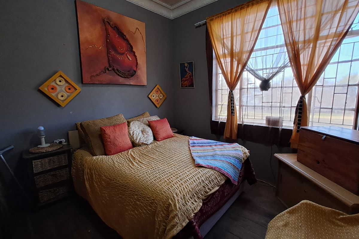 A bedroom featuring dark-toned walls, decorative cornice detailing, and large windows fitted with security bars.