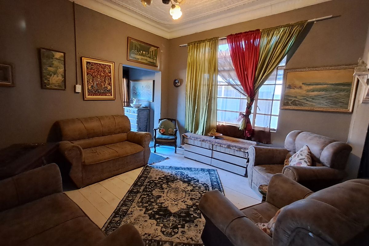 A living room featuring original ornate ceiling details and timber flooring, offering a character-filled space with potential for cosmetic updates.
