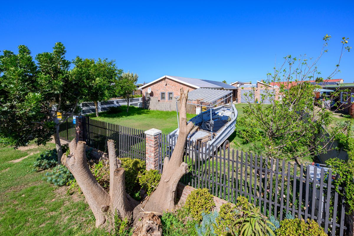 A rear view of a brick house featuring a large lawn, metal perimeter fencing, and solar panels installed on the roof.