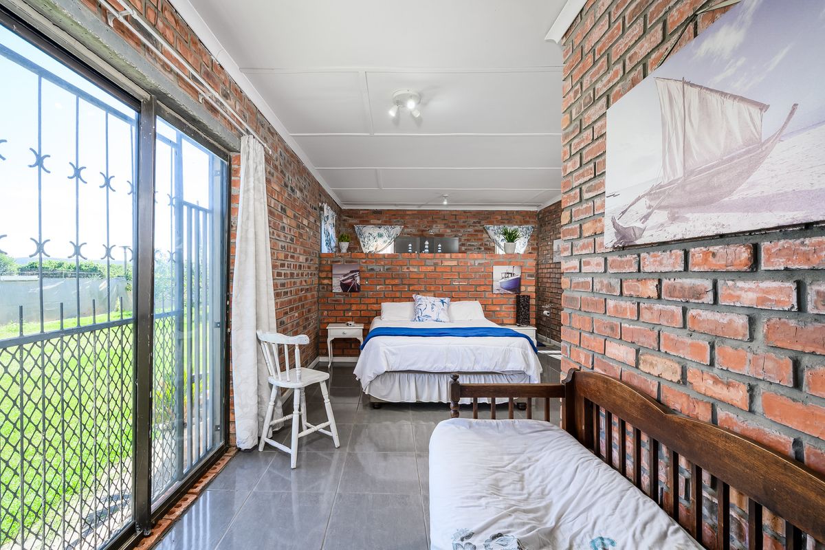 A bedroom featuring exposed brick walls, tiled flooring, and a sliding glass door with security gate providing access to the exterior.