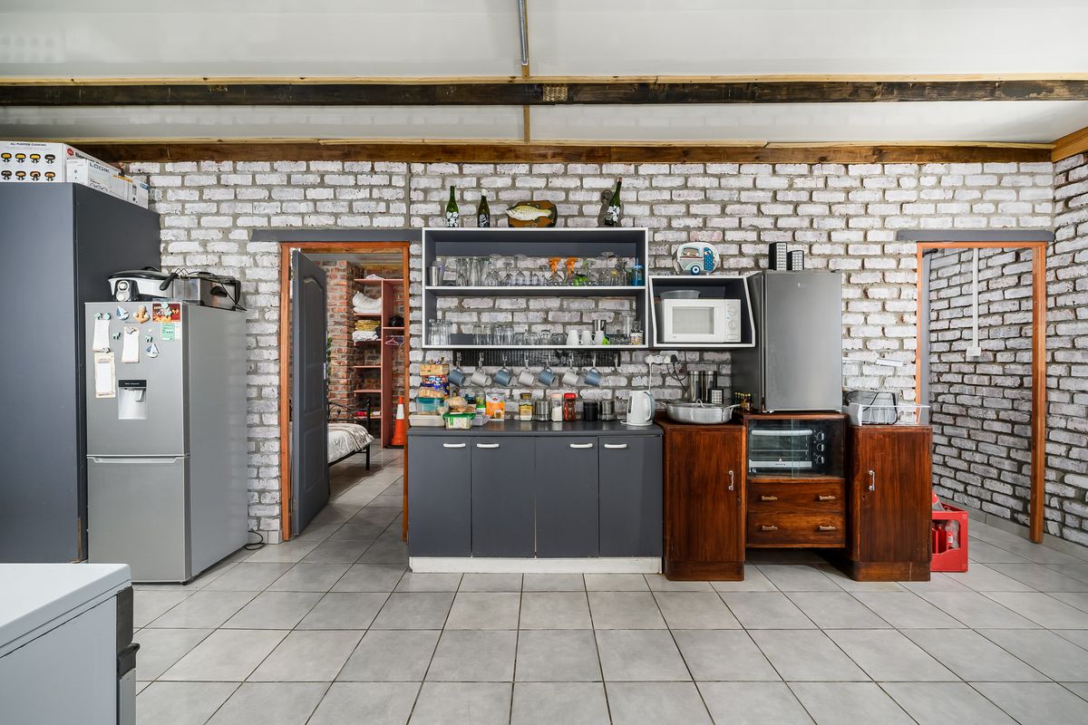 A rustic kitchen area featuring exposed brick walls, timber ceiling beams, tiled flooring, and a mix of modern and traditional built-in cabinetry.