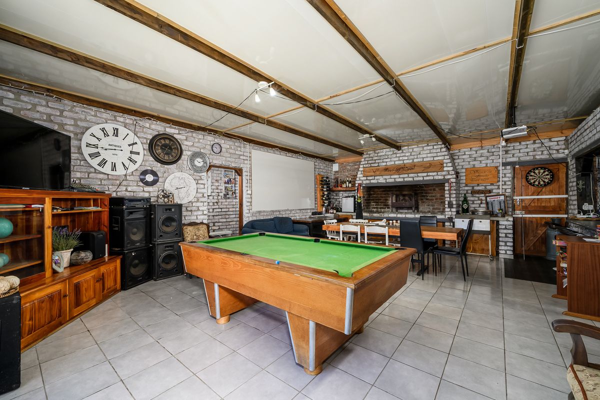 Spacious entertainment area featuring exposed brick walls, timber ceiling beams, and a built-in brick fireplace, currently utilized as a games room.