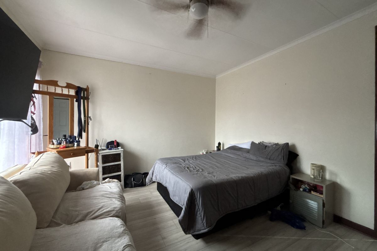 A functional bedroom featuring laminate flooring, a ceiling fan, and neutral wall finishes, offering a blank canvas for potential interior updates.