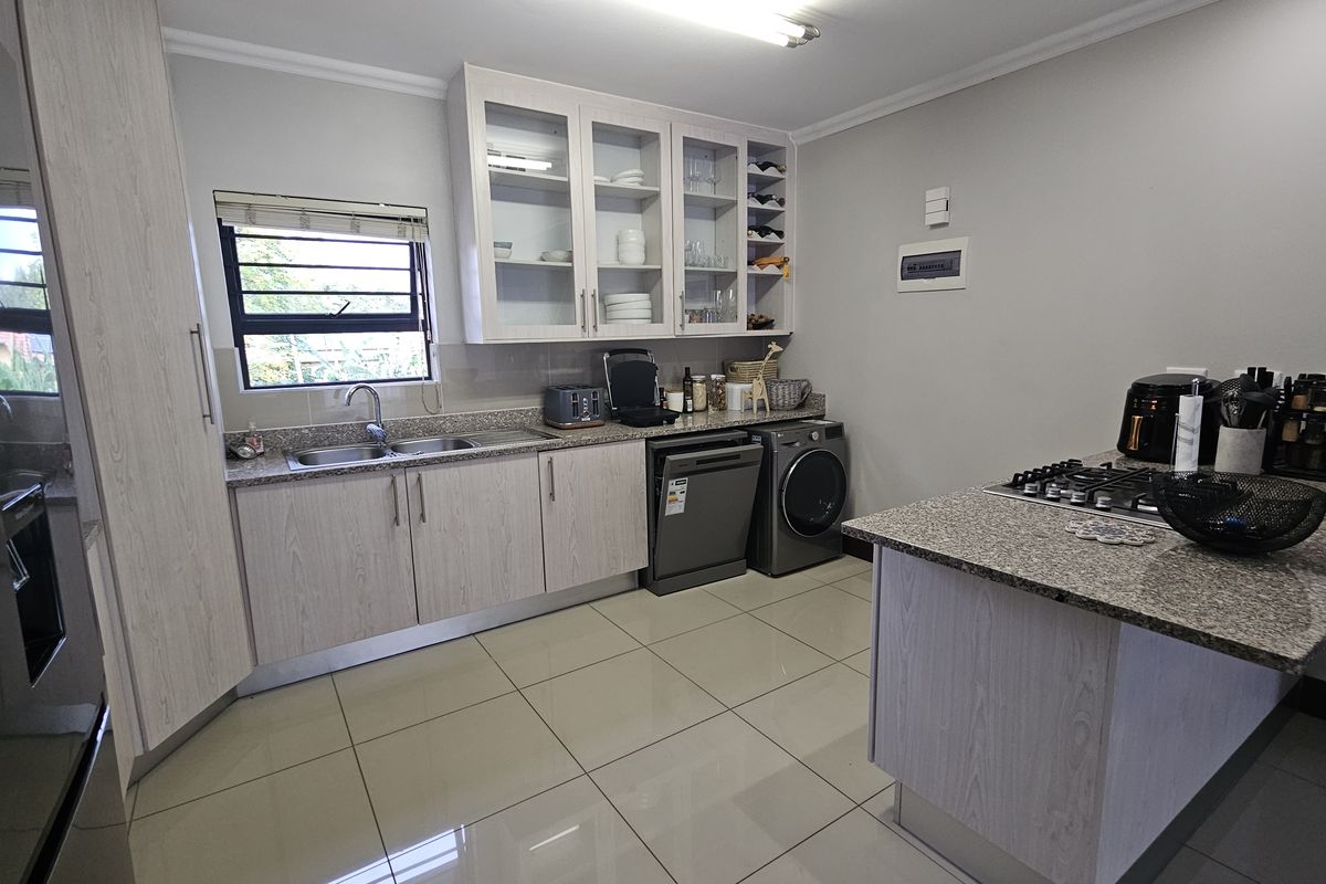 Modern kitchen featuring light wood-grain cabinetry, granite countertops, a gas hob, and integrated storage with glass-front display cabinets and tiled flooring.