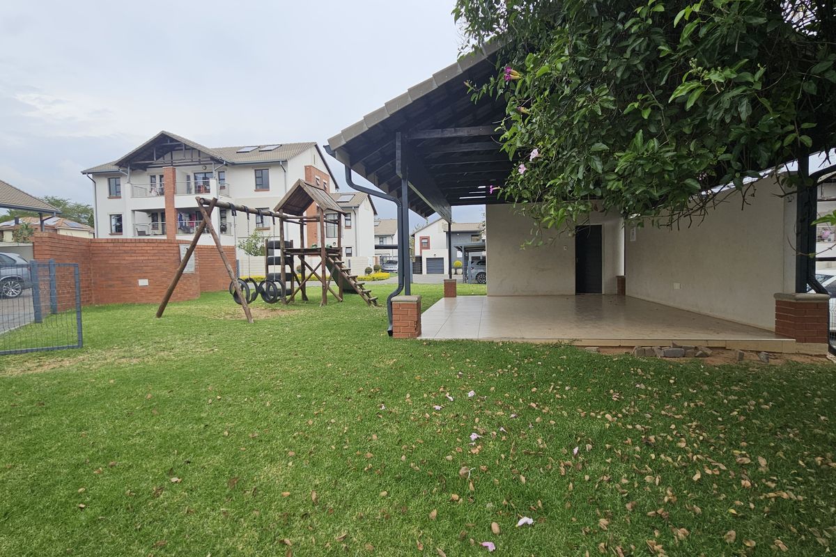 A spacious rear garden area featuring a covered patio with tiled flooring, brick boundary walls, and a well-maintained lawn.
