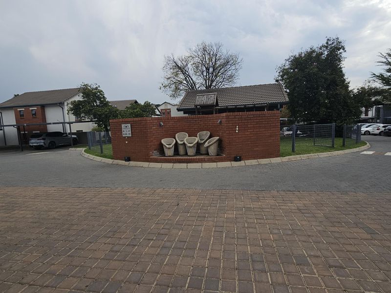 View of the apartment complex entrance featuring a brick boundary wall, paved driveway, and established landscaping.