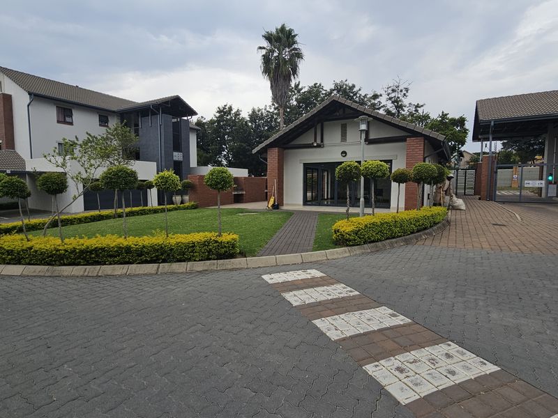A well-maintained apartment complex entrance featuring paved driveways, landscaped gardens, and secure gated access.