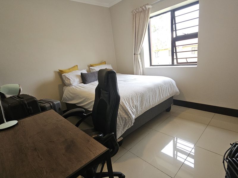 A well-maintained bedroom featuring neutral tiled flooring, a large window with security bars, and built-in storage cabinetry.