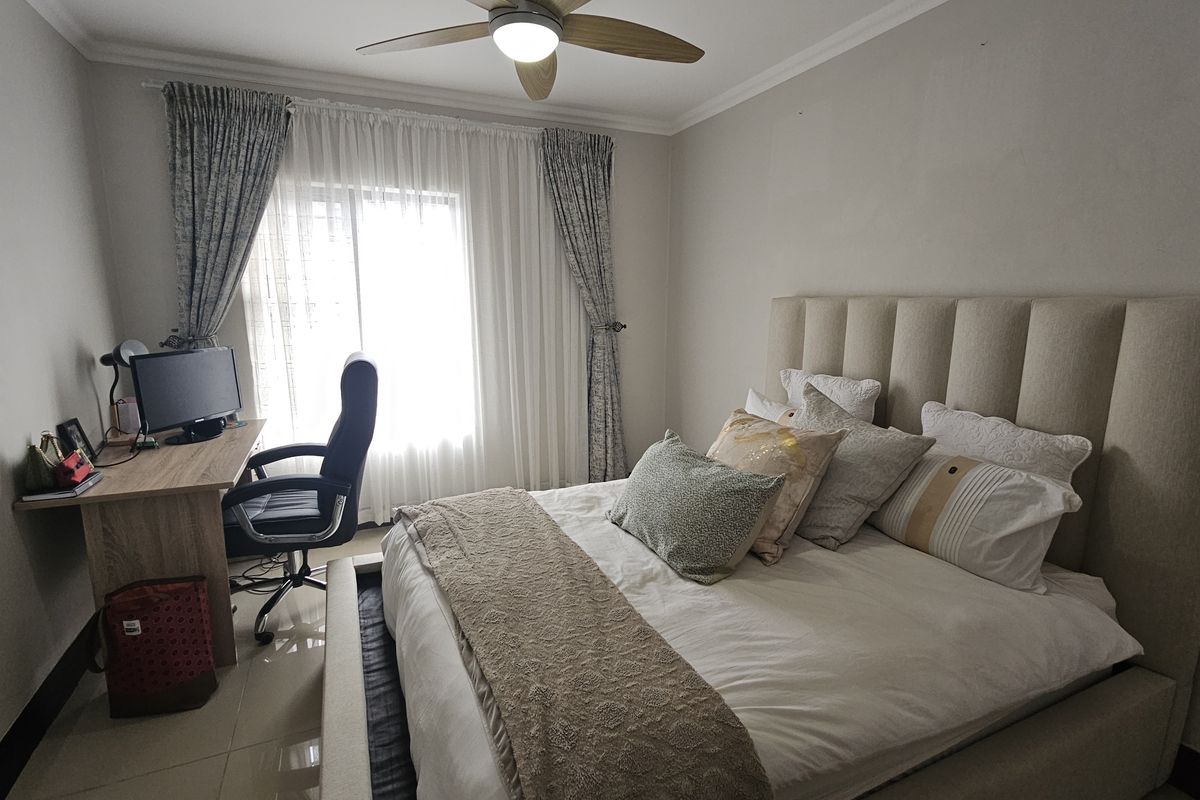A well-maintained bedroom featuring tiled flooring, a ceiling fan, and a large window with curtains, providing a comfortable and functional living space.
