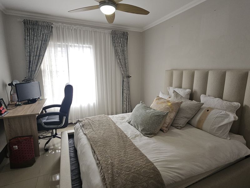 A well-maintained bedroom featuring tiled flooring, a ceiling fan, and a large window with curtains, providing a comfortable and functional living space.