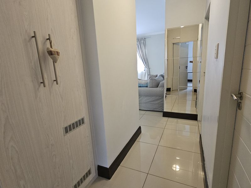 A clean, well-maintained hallway featuring tiled flooring, a built-in cupboard with modern handles, and a decorative mirrored wall panel.