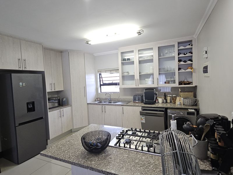 A functional kitchen featuring light wood-finish cabinetry, granite countertops, a gas hob, and integrated storage including a wine rack.