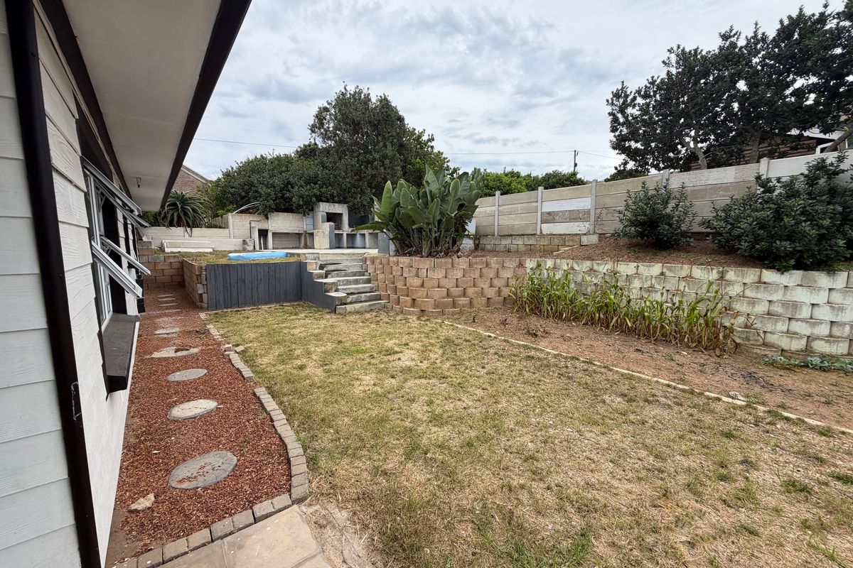 A rear garden featuring tiered landscaping with concrete retaining walls, a built-in outdoor braai area, and a lawn space.