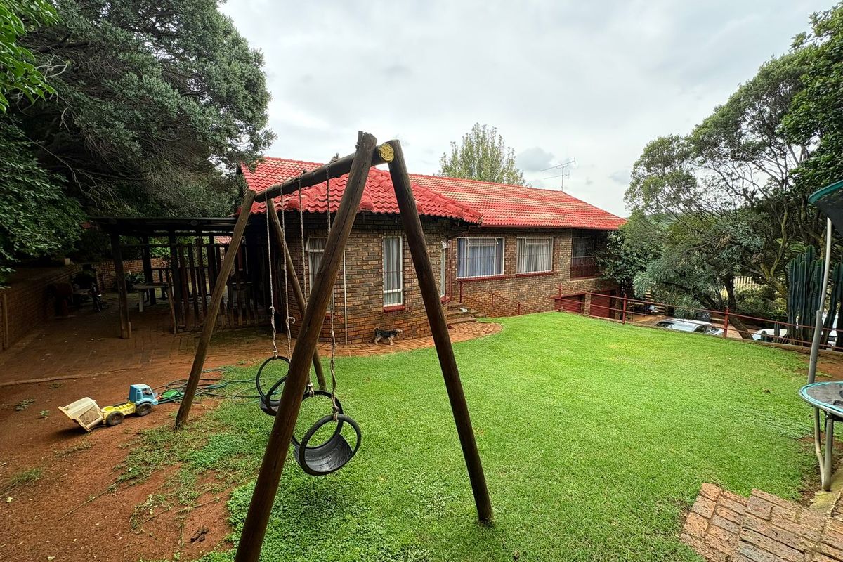 Rear view of a brick-faced house featuring a tiled roof, a covered patio area, and a spacious garden with established trees.