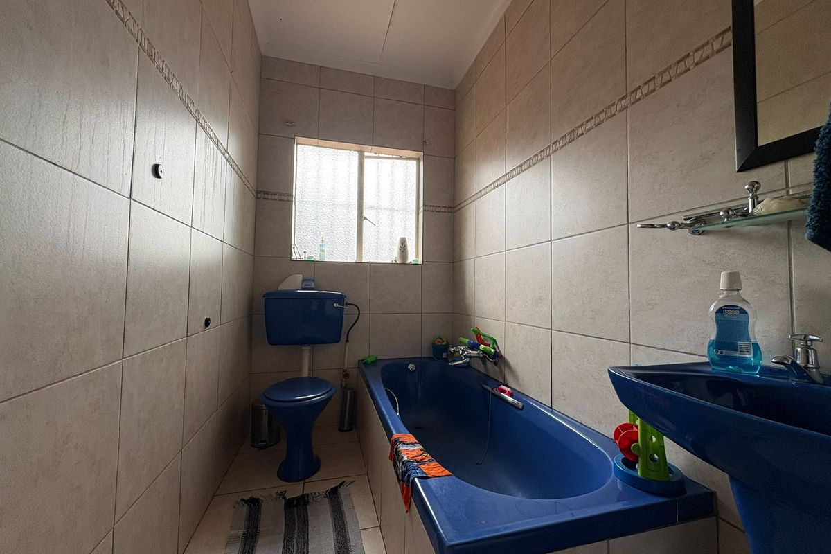 A compact bathroom featuring floor-to-ceiling wall tiles, a blue bathtub, a matching blue toilet, and a blue pedestal basin.