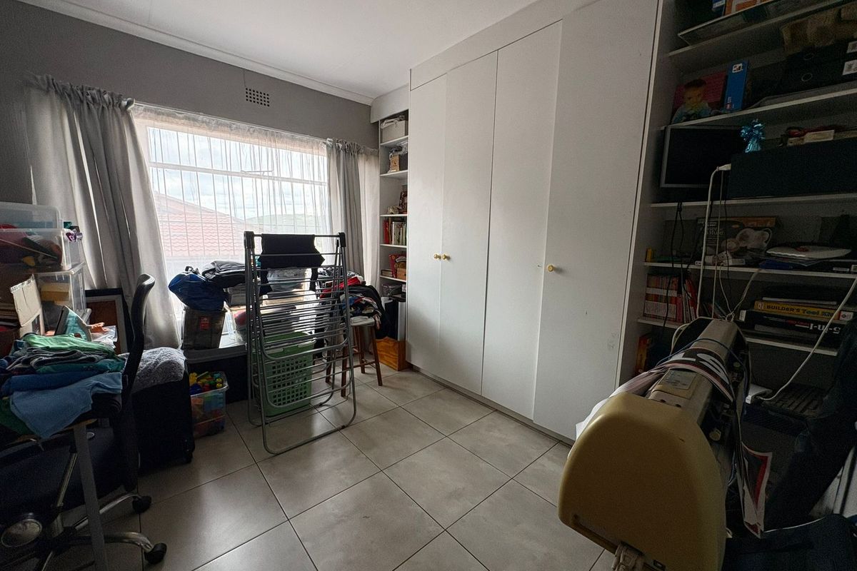 A bedroom featuring built-in cupboards, tiled flooring, and a large window providing natural light.
