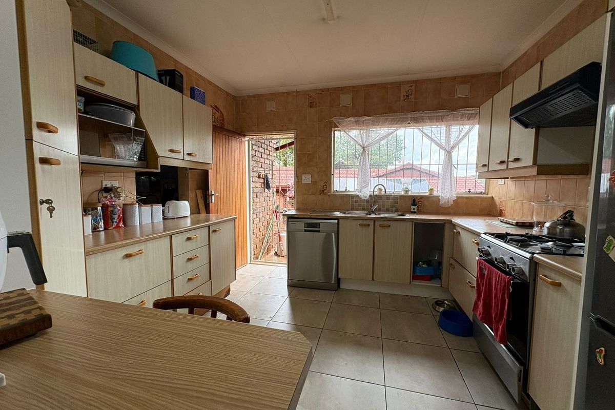 A functional kitchen featuring light-toned cabinetry, tiled splashbacks, a gas stove with extractor fan, and direct access to the exterior.