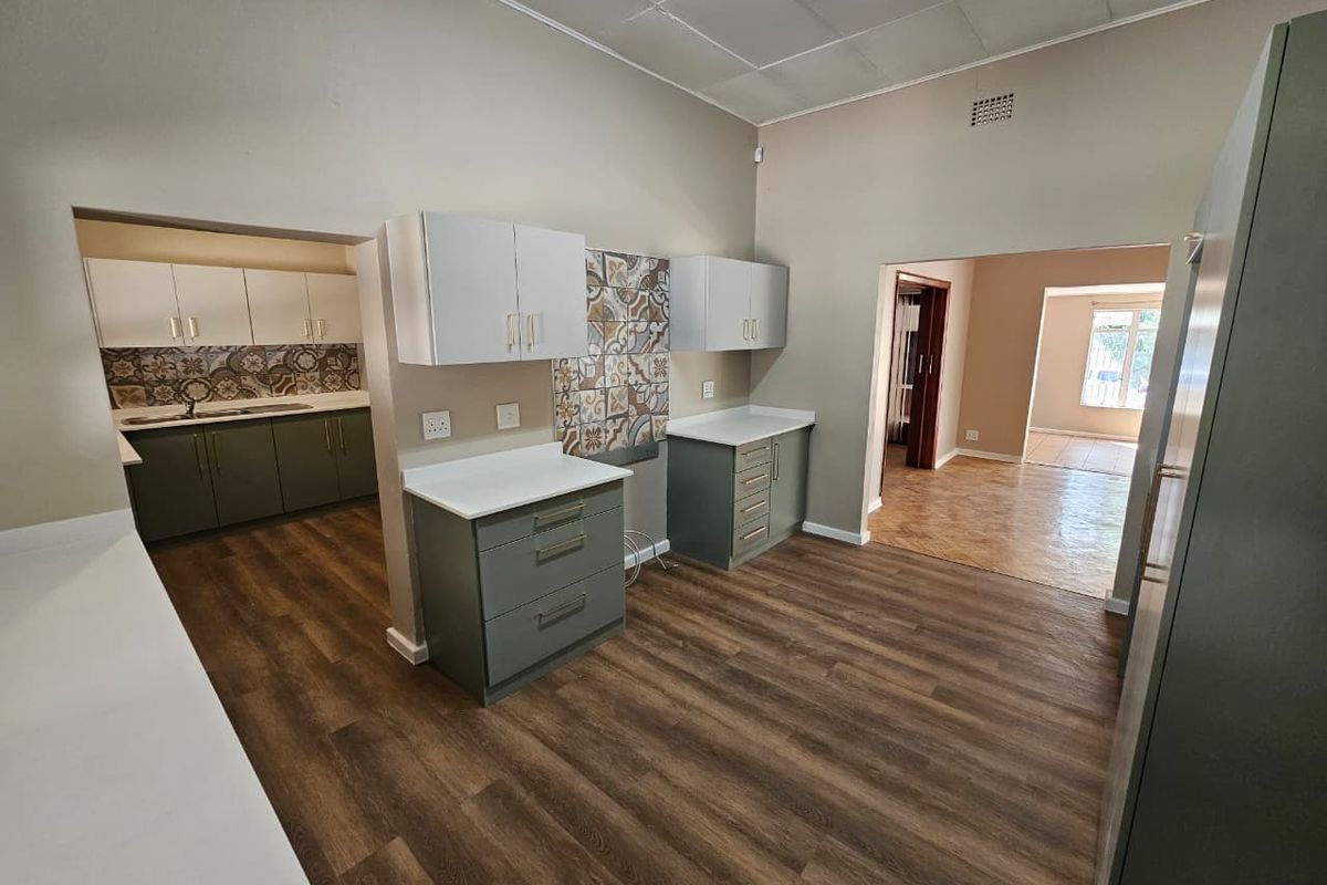 A spacious kitchen featuring modern olive green cabinetry, white countertops, and decorative patterned tile backsplashes, with an open-plan layout connecting to adjacent living areas.