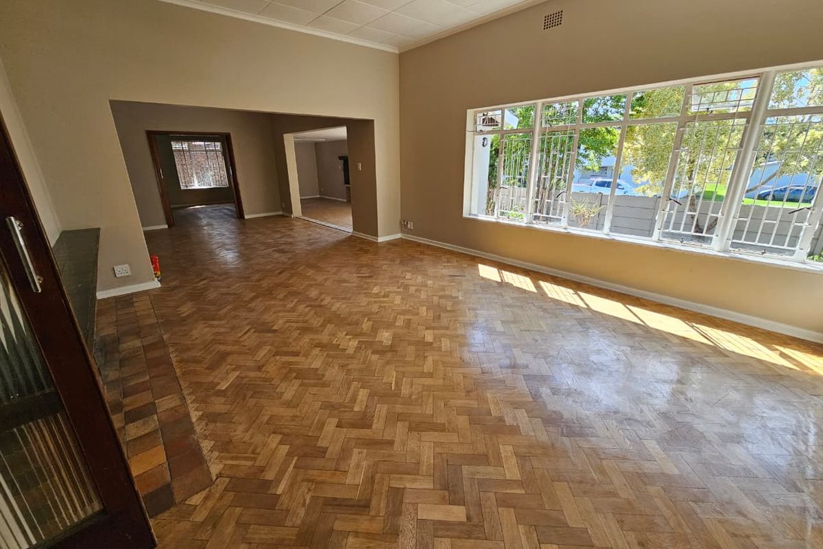 Spacious living area featuring classic herringbone parquet flooring, large windows with security bars, and an open-plan layout connecting to adjacent rooms.